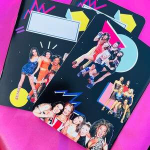 K&ouml;nnte beinhalten: Drei schwarze Notizb&uuml;cher mit farbenfrohen geometrischen Designs und Bildern einer Popmusikgruppe. Die Notizb&uuml;cher haben einen wei&szlig;en rechteckigen Bereich f&uuml;r einen Namen oder Titel. Der Hintergrund ist hellrosa.