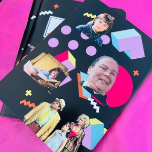 K&ouml;nnte beinhalten: Schwarze Notizb&uuml;cher mit Bildern von Charakteren aus dem Film "Matilda" und farbenfrohen geometrischen Formen. Die Notizb&uuml;cher haben einen rosa Hintergrund. Das Design umfasst rosa Kreise, blaue und violette W&uuml;rfel sowie gelbe und orangefarbene Formen.