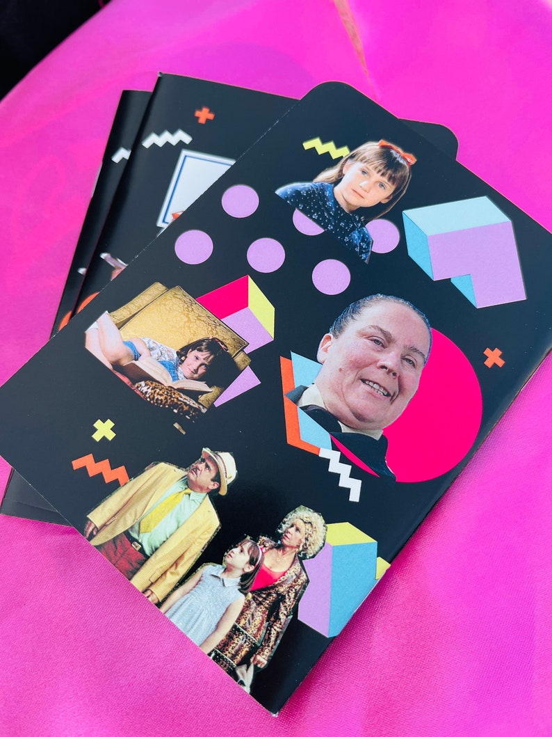 K&ouml;nnte beinhalten: Schwarze Notizb&uuml;cher mit Bildern von Charakteren aus dem Film "Matilda" und farbenfrohen geometrischen Formen. Die Notizb&uuml;cher haben einen rosa Hintergrund. Das Design umfasst rosa Kreise, blaue und violette W&uuml;rfel sowie gelbe und orangefarbene Formen.