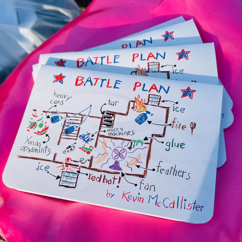 K&ouml;nnte beinhalten: Ein Stapel wei&szlig;er Papierbl&auml;tter mit einer handgezeichneten "BATTLE PLAN"-Zeichnung. Der Plan enth&auml;lt beschriftete Illustrationen von "heavy cans", "tar", "fire" und "Xmas ornaments". Der Name des K&uuml;nstlers, "Kevin McCallister", steht unten.