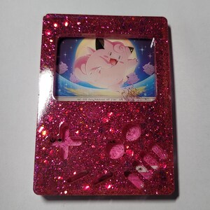 May include: Pink glitter resin Game Boy with a clear frame and a Jigglypuff Pokemon card inside. The card shows Jigglypuff floating in the air with a moon and stars in the background. The text on the card reads "NO. 035 Fairy Pokemon HT: 2'00" WK: 19.8 lbs."