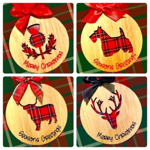 May include: Four round wooden ornaments with red and black plaid designs. The ornaments feature a thistle, a terrier, a highland cow, and a reindeer. The ornaments are decorated with the text "Merry Christmas" and "Seasons Greetings".