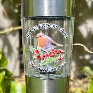 Könnte beinhalten: Ein klares Glas-Solarlicht mit einem Rotkehlchen auf einem Zweig mit roten Beeren. Das Licht trägt den Text "Rotkehlchen erscheinen, wenn geliebte Menschen in der Nähe sind".