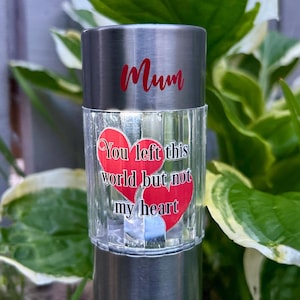 Könnte beinhalten: Silberne Solar-Gartenleuchte mit dem Wort "Mum" in roter Schrift. Der transparente, strukturierte Glasteil zeigt zwei rote Herzen und den Text "You left this world but not my heart."