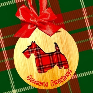 May include: A wooden Christmas ornament with a red and black plaid dog silhouette and the text "Seasons Greetings". The ornament is decorated with a red bow.