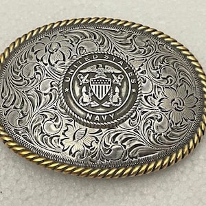 May include: Silver belt buckle with an ornate floral design and a United States Navy emblem in the center. The buckle is surrounded by a gold-colored border.