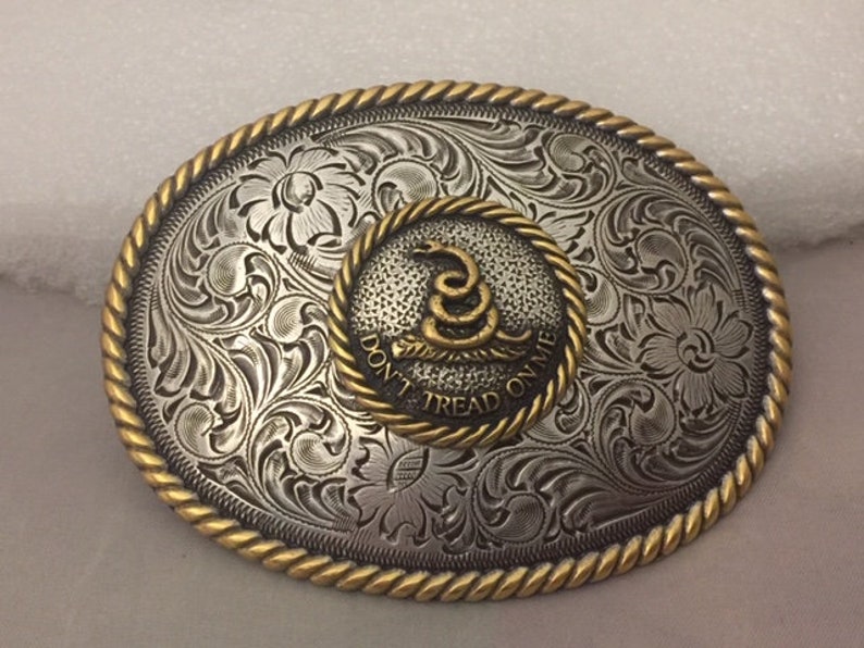 May include: Silver belt buckle with a gold-toned border and a circular inset featuring a coiled snake with the text "Don't Tread On Me".