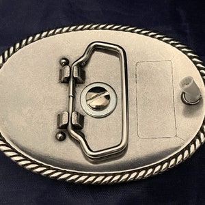 Puede incluir: Hebilla de cintur&oacute;n de plata con un borde de dise&ntilde;o de cuerda. La hebilla tiene un bucle de metal y un peque&ntilde;o pasador de metal en el lateral.
