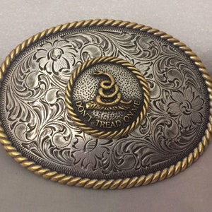 May include: A silver and gold belt buckle with an engraved floral design. The center of the buckle features a gold snake with the words "Don't Tread On Me".