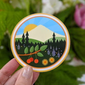 May include: A round sticker with a colorful illustration of a mountain landscape with trees, flowers, and cherries. The sticker has a white border and a yellow background.