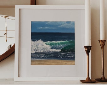 May include: A framed painting of a blue ocean wave crashing on a sandy beach. The painting is in a white frame and is hanging on a white wall.