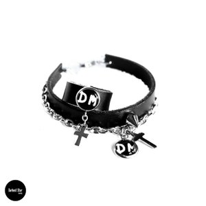 May include: Black leather choker necklace with silver chain and two silver charms. The charms are round and have the letters "DM" on them. There are also two silver cross charms.