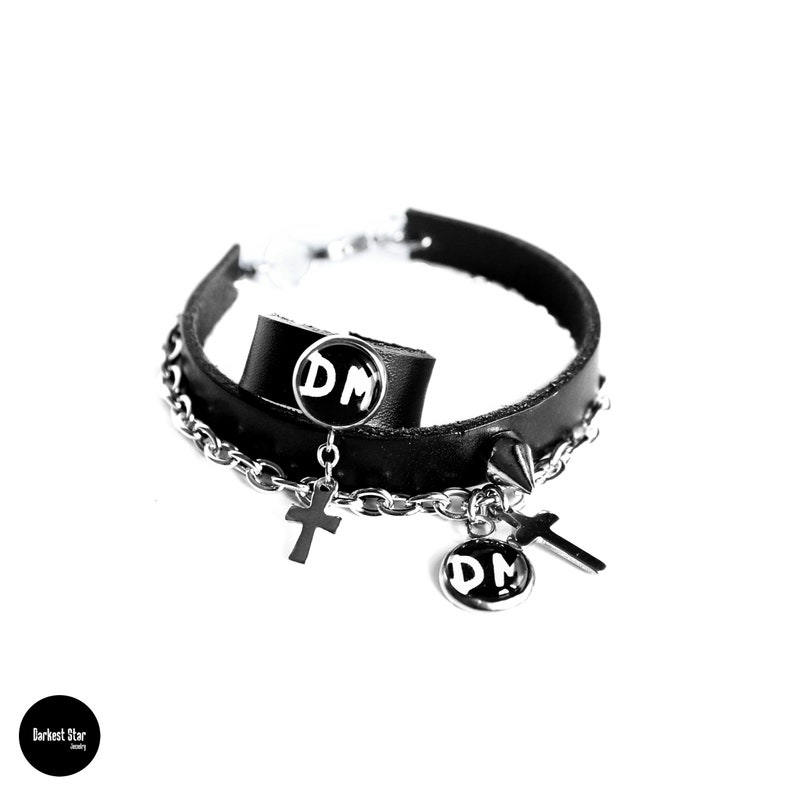 May include: Black leather choker necklace with silver chain and two silver charms. The charms are round and have the letters "DM" on them. There are also two silver cross charms.