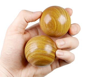 May include: Two wooden balls with a brown and yellow striped pattern are held in a person's hand.