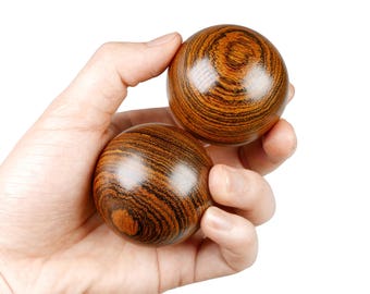 May include: Two brown wooden balls with a striped pattern are held in a person's hand. The balls are used for exercise and relaxation.