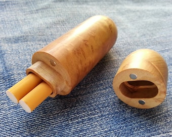 May include: A wooden cigarette case with a magnetic closure. The case is open and two cigarettes are inside. The case is made of light brown wood with a natural grain pattern.