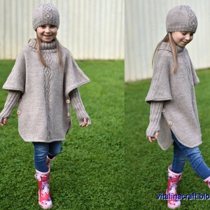 May include: A child wearing a beige knitted poncho with a cable knit pattern, matching beige knitted hat, and pink rain boots. The poncho has long sleeves and a high neck.