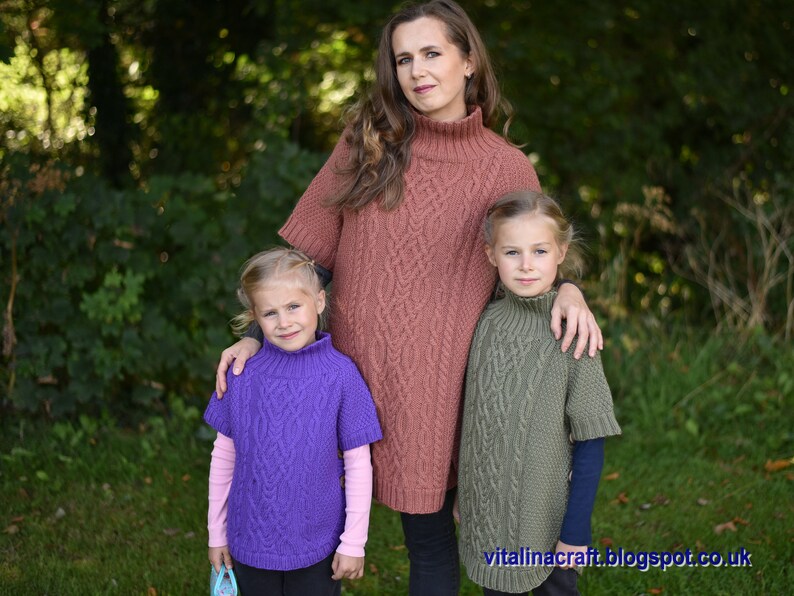 May include: A woman and two girls wearing matching cable knit sweaters in different colors. The woman is wearing a rust colored sweater, the older girl is wearing a green sweater, and the younger girl is wearing a purple sweater. All three sweaters have a high neck and short sleeves.