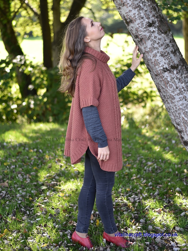 K&ouml;nnte beinhalten: Eine Frau tr&auml;gt einen rostigen Strickponcho mit Rollkragen, eine dunkle Jeans und rote Schuhe. Sie steht in einem grasbewachsenen Bereich mit heruntergefallenen Bl&auml;ttern und einem Baumstamm hinter ihr.
