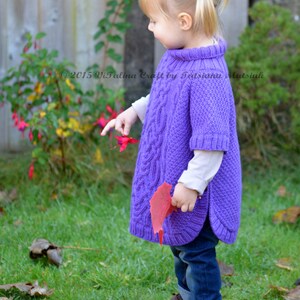 May include: A young girl wearing a purple knitted poncho with a cable knit pattern. She is standing in a grassy area with fall leaves on the ground. The text "2015 Vitalina Craft by Tetiana Matsiuk" is visible in the image.