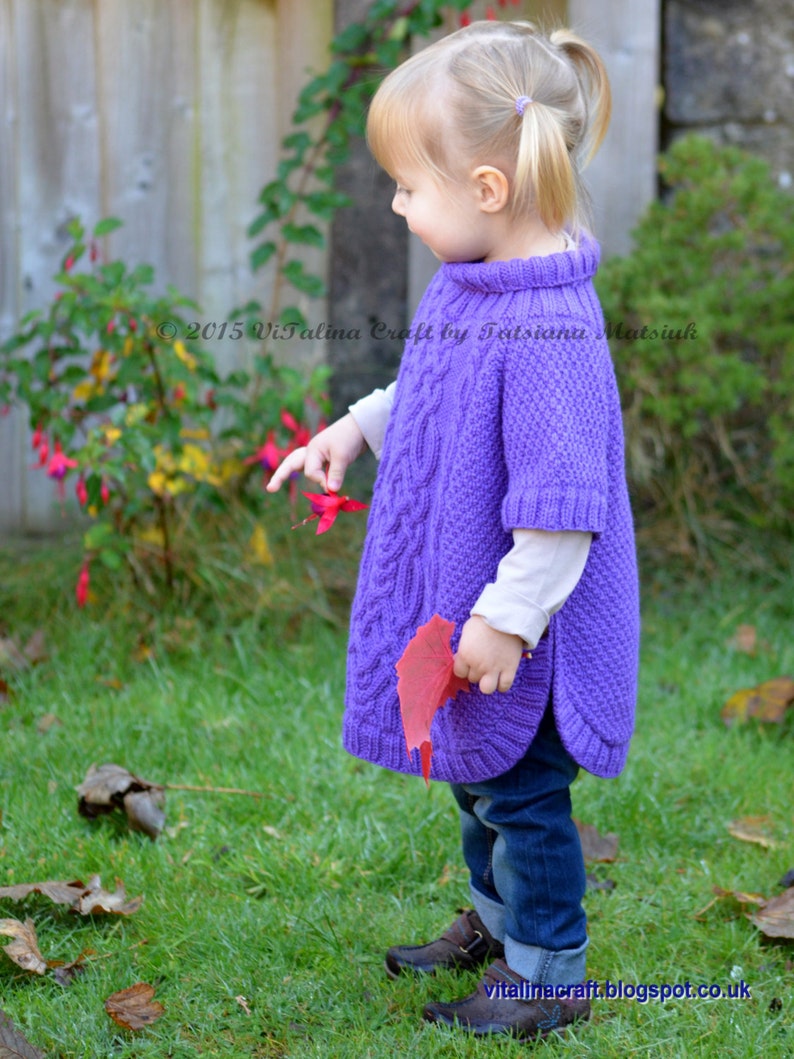 May include: A young girl wearing a purple knitted poncho with a cable knit pattern. She is standing in a grassy area with fall leaves on the ground. The text "2015 Vitalina Craft by Tetiana Matsiuk" is visible in the image.