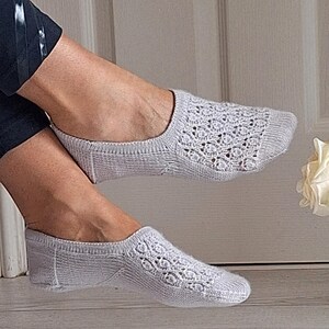 May include: A pair of pale grey, open-weave socks. The socks feature a delicate, lacy pattern on the top of the foot. The socks are designed to be worn discreetly. The socks are made of a soft, knitted material.