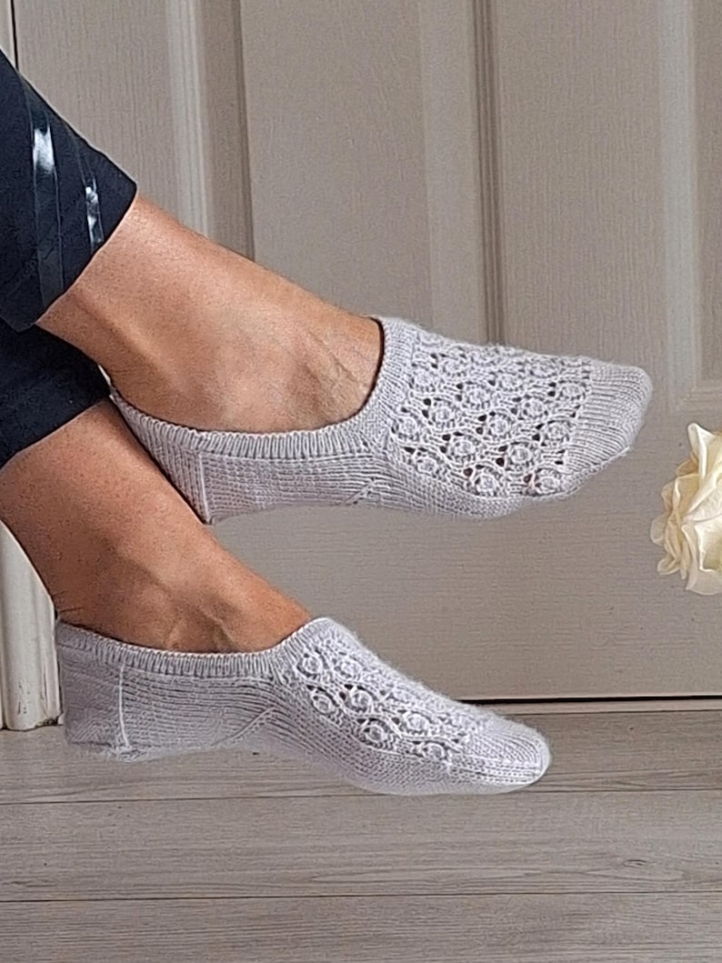 May include: A pair of pale grey, open-weave socks. The socks feature a delicate, lacy pattern on the top of the foot. The socks are designed to be worn discreetly. The socks are made of a soft, knitted material.