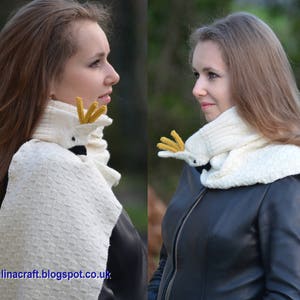 May include: Two women wearing white knitted scarves with a bird design. The scarves are white with a yellow beak and black eyes. The women are wearing black leather jackets.
