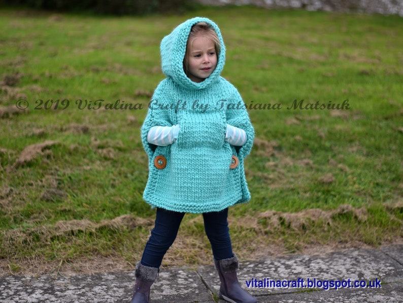 May include: A turquoise knitted hooded poncho with a pocket and wooden buttons. The poncho is worn by a child standing on a path.