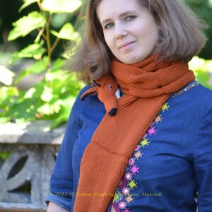 May include: A woman wearing a blue denim shirt with colorful embroidery and a knitted fox scarf. The scarf is orange with white accents and has a fox head at the end.