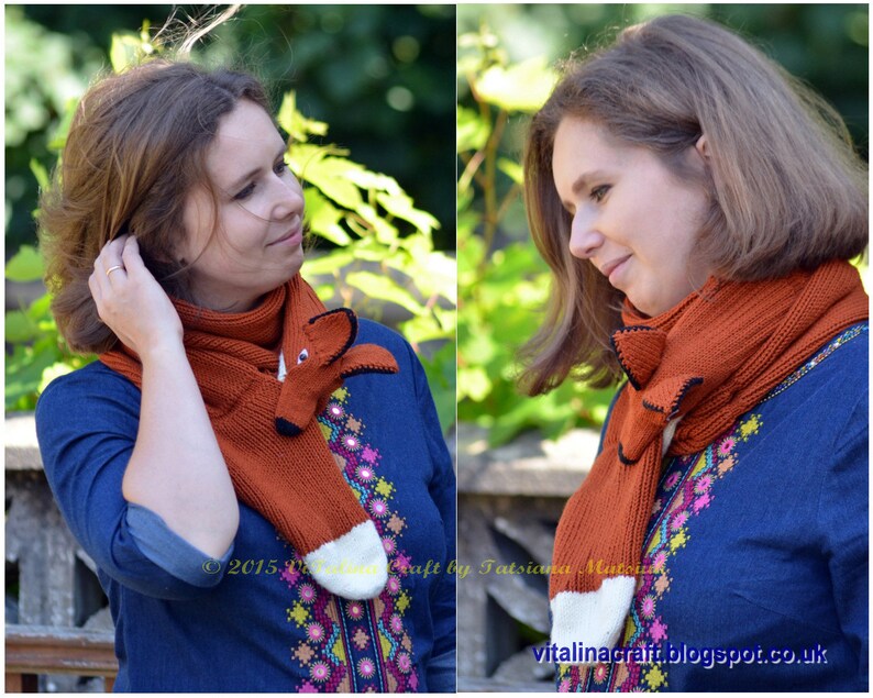 May include: A woman is wearing a knitted fox scarf in orange and white. The scarf has a fox head with black eyes and a black nose. The woman is wearing a blue shirt with colorful embroidery.