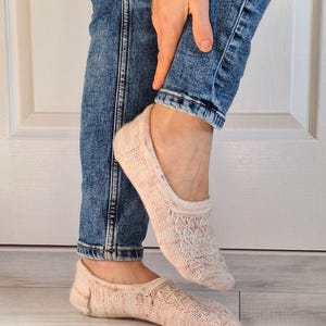 May include: A pair of pink and white patterned ankle socks with a lacy design. The socks are being worn on a person's feet.