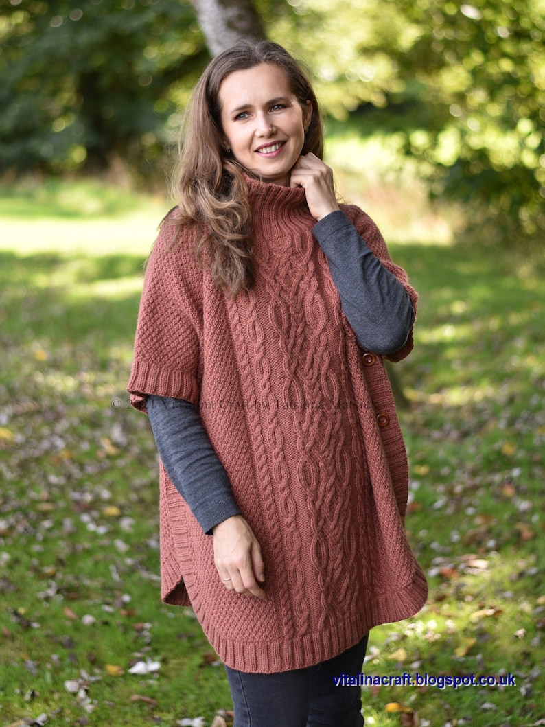 K&ouml;nnte beinhalten: Ein rostiger Strickponcho mit Zopfmuster und hohem Kragen. Der Poncho hat einen Knopfverschluss an der Seite.