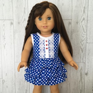 May include: A doll wearing a blue and white polka dot dress with a white lace trim and red buttons. The doll has long brown hair and blue eyes. The dress has a ruffled skirt.
