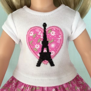 Puede incluir: Camiseta blanca con un parche rosa en forma de coraz&oacute;n que presenta una silueta negra de la Torre Eiffel. El parche en forma de coraz&oacute;n tiene un patr&oacute;n floral.