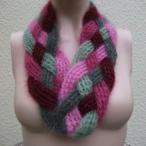 May include: A braided knit scarf in shades of pink, burgundy, and grey. The scarf is made of a soft, fuzzy yarn and is perfect for keeping warm in the winter.
