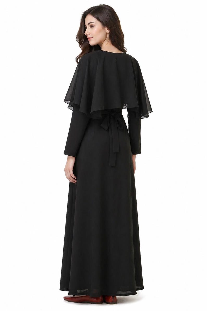 May include: A long black dress with a matching cape. The dress has long sleeves and a flowing skirt. The cape is a sheer, layered design that drapes over the shoulders. A black tie belt cinches the waist. The dress is suitable for formal events.