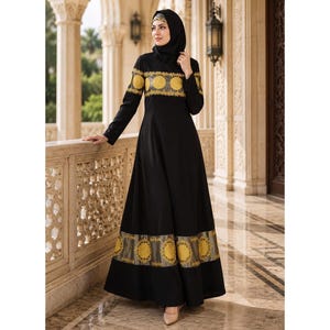 May include: A floor-length black long-sleeve dress featuring a solid black bodice and skirt accented by two horizontal bands of gold circular patterns. The dress is paired with a matching black head covering that frames the face.