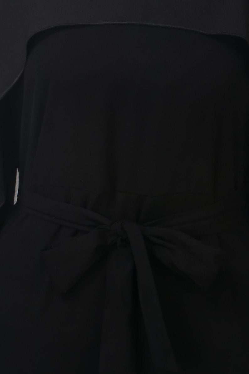 May include: A close-up of a black dress with a tied waist. The dress is made of a smooth fabric and features a bow detail at the waist. The dress appears to be a solid color, with no visible patterns or embellishments.