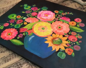 May include: A vibrant floral painting featuring a blue vase overflowing with colorful blooms. The arrangement includes pink, orange, yellow, and green flowers, set against a dark blue background. The artwork is displayed on a square canvas.