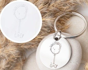 May include: A silver keychain with a round charm featuring a child's drawing of a person with the word "dad" underneath. The drawing is engraved on the charm.