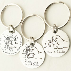 May include: Three silver keychains with round metal tags featuring a fist bump design and personalized text. The text on the tags reads "Flizeleth. Joey, Emily, inaiso. Steve, Williem & Deddy", "Katie, Lucy Esmee & Daddy", and "Rex & Daddy".