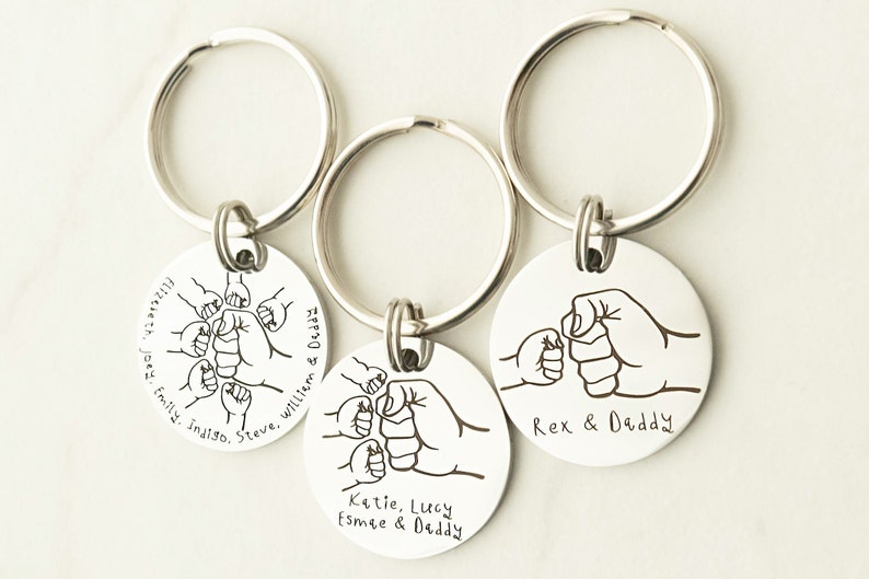 May include: Three silver keychains with round metal tags featuring a fist bump design and personalized text. The text on the tags reads "Flizeleth. Joey, Emily, inaiso. Steve, Williem & Deddy", "Katie, Lucy Esmee & Daddy", and "Rex & Daddy".