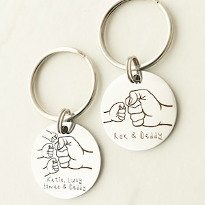 May include: Two silver keychains with engraved fist bump designs. One keychain has the text "Rex & Daddy" and the other has the text "Katie, Lucy, Esmee & Daddy".