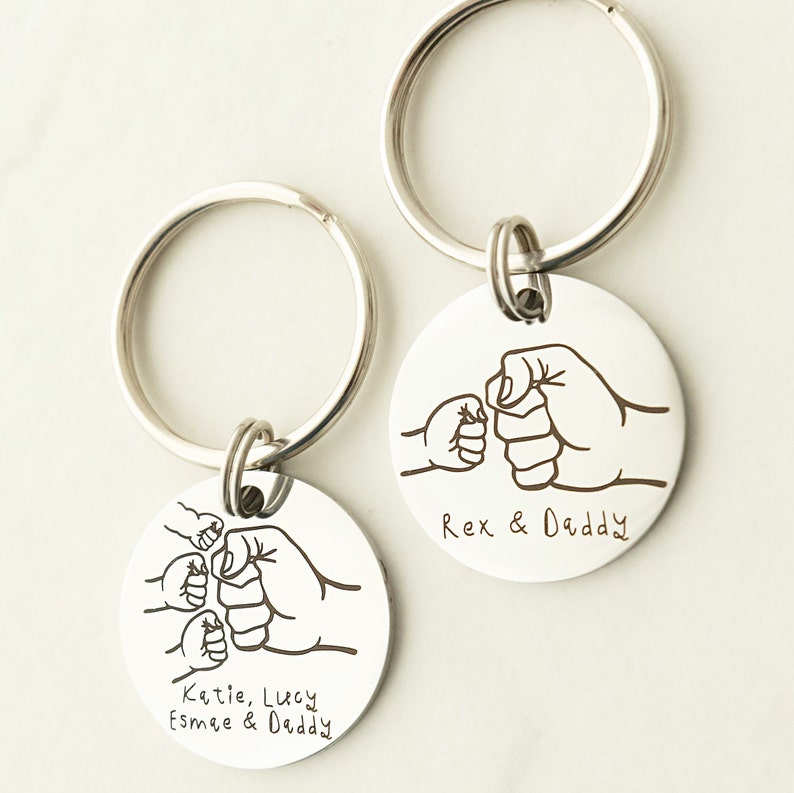May include: Two silver keychains with engraved fist bump designs. One keychain has the text "Rex & Daddy" and the other has the text "Katie, Lucy, Esmee & Daddy".