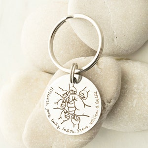 May include: Silver keychain with a round tag featuring a fist bump design and the names "Elizabeth, Joey, Emily, Indigo, Steve, William & Daddy".