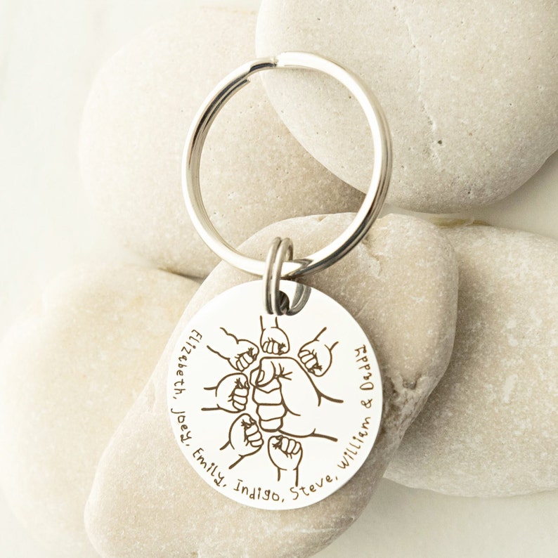 May include: Silver keychain with a round tag featuring a fist bump design and the names "Elizabeth, Joey, Emily, Indigo, Steve, William & Daddy".