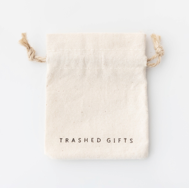 Pode incluir: Uma bolsa de algod&atilde;o branco com cord&atilde;o de ajuste, com o texto "TRASHED GIFTS" impresso na frente.