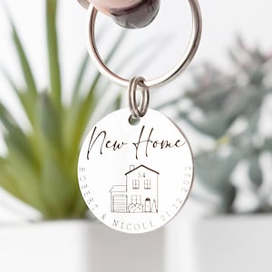 May include: Silver keychain with a round tag that says "New Home" with a house illustration and the names "Robert & Nicole" and the date "21.12.2022".