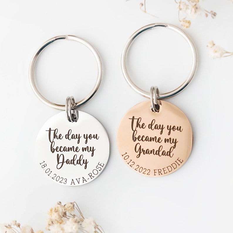 30mm rose gold engraved keyring from trashed gifts alongside a 30mm stainless steel engraved keyring. Text reads The day you became my Daddy and is customisable with a child's name and date of birth around the bottom curve of the disc.